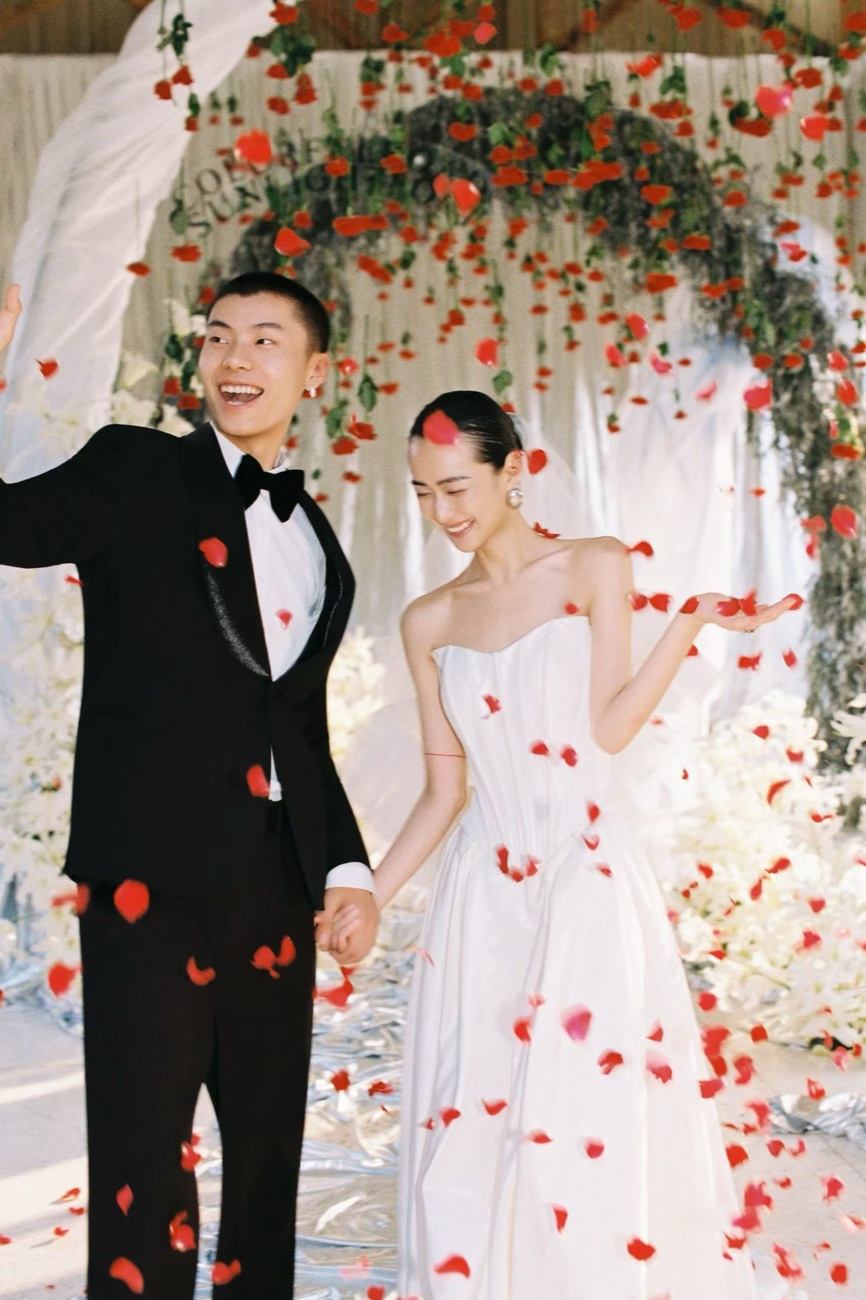 A newlywed couple under a rose-petal arch, the bride in a Lichée Bridal gown